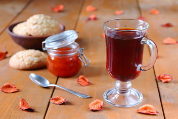 A glass mug of black tea with a glass bowl of homemade peach jam on a wooden table among autumn decor. 