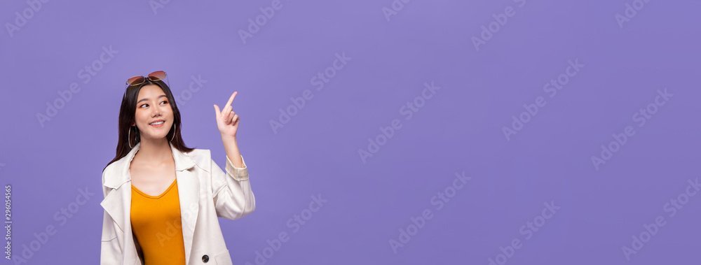 Wall mural asian girl pointing hand to empty space on purple banner background