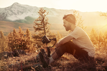 Man sits with gimbal and camera against mountains