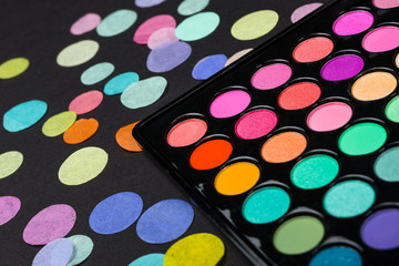 Close-up of eyeshadow palette on a black background with scattered confetti. Macro shot of eyeshadow palette