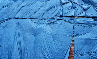 blue plastic tarpaulin protecting an old brick wall which is about to be refurbished. Abstract background - obrazy, fototapety, plakaty