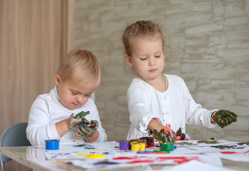 Little children paint with paints. The kids got their hands dirty in gouache. A cute girl and a boy...