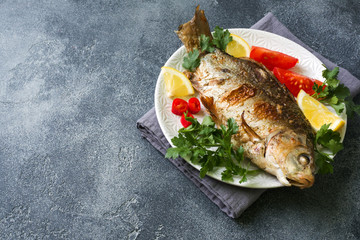 Baked carp fish with vegetables and spices on a plate on a dark table with a copy of space.