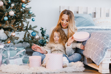 mother and beautiful blonde baby girl opening presents next to the christmas tree