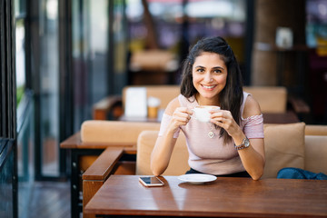 Young woman with smartphone holding cup coffee in a cafe