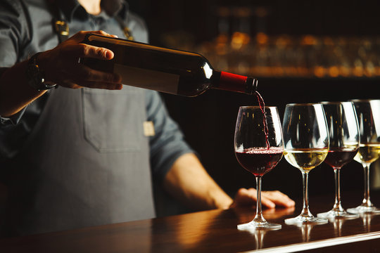 Bartender pours red wine in glasses on wooden bar counter
