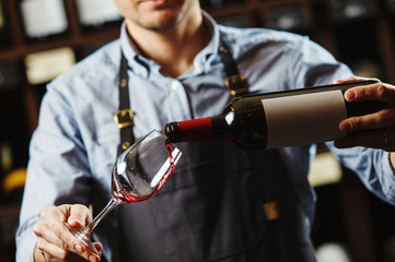 Male sommelier pouring red wine into long-stemmed wineglasses.