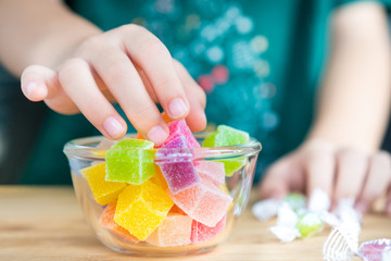 Closeup hands of a little child taking a piece of jelly cube with sugar in a glass bowl. Snacks...