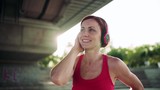 Young woman with headphones resting after doing exercise outdoors in city.