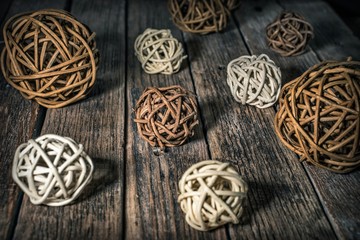 Dark and light decorative rattan balls of different sizes lie on a wooden surface