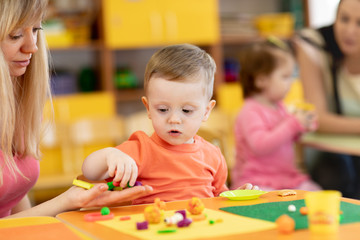 Fototapeta premium Little kid boy learning to use colorful play clay in kindergarten. Babies group studying in creche or nursery