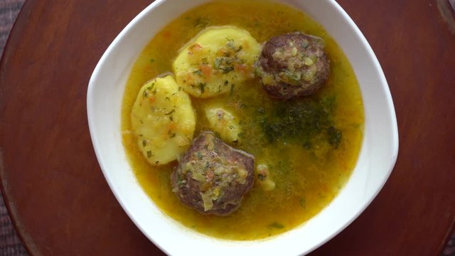 Sopa de alb&oacute;ndigas y papa hervida rotando sobre plataforma de madera en una mesa