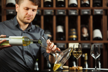 Male sommelier pouring white wine in decanter