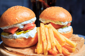 Two fish burgers with pieces of fish and fries. Burgers on a dark background.