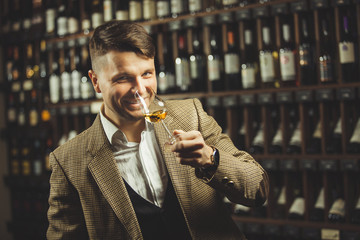 Smiling sommelier in the wine cellar tasting whiskey. - obrazy, fototapety, plakaty