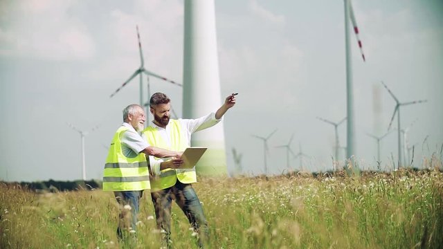Engineers standing on wind farm, making notes. Slow motion.