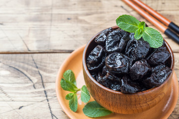 Bowl with tasty dried plums on wooden table Copy space