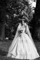 Portrait of a beautiful bride in veil with a bouquet of flowers in the park. Black and white