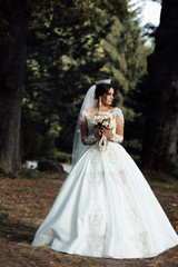 Fototapeta premium Happy bride in a beautiful dress walking in the park. Happy wedding. Young beautiful stylish woman, bride, bridal fashion, summer trend, flowers, roses, hairstyle, beauty make-up, white dress. 