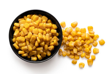 Canned sweet corn in a black ceramic bowl next to spilled sweet corn isolated on white. Top view.
