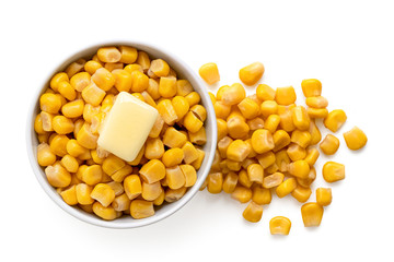 Canned sweet corn with a knob of butter in a white ceramic bowl next to spilled sweet corn isolated on white. Top view.