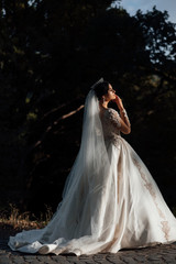 Sunshine photo of happy bride outdoor in nature location at sunset. Warm summertime. Happy bride in a beautiful dress walking in the park. Woman waiting for the groom
