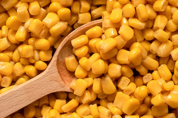 Background of canned sweet corn with wooden spoon. Top view.