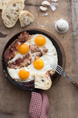 Fried eggs in iron pan fork knife - traditional rustic breakfast. Top view pan of fried eggs, sausage for breakfast on wooden table background.