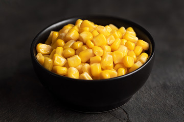 Canned sweet corn in a black ceramic bowl isolated on black slate.