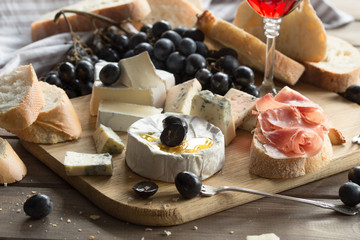 different varieties of cheese with fruits, nuts, dried fruits and kitchen utensils for cheese plate, nuts, dried fruits, wine and kitchen utensils for cheese plate