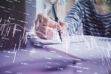 Financial forex graph drawn over hands taking notes background. Concept of research. Double exposure