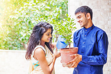 Beautiful Indian couple watering the plant in the garden on their balcony at home