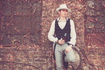 Fedora styled man with beer bottle against the wall.