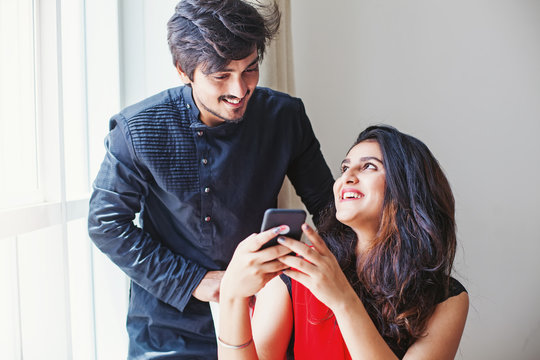 Indian man and woman using mobile phone together and smiling happily