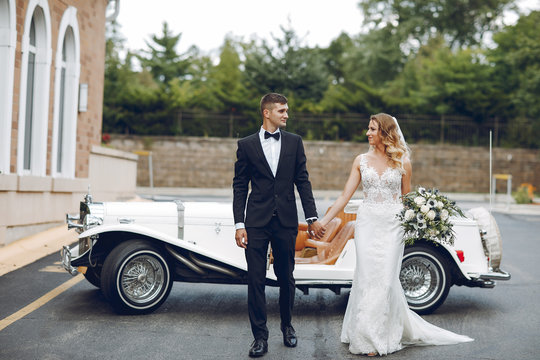 Beautiful Bride In A Long White Dress. Handsome Groom In A Black Suit. Couple Near Old Car