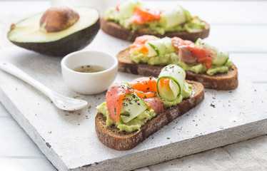 sandwich with avocado and salmon on a light background, green onions and gluten-free grain bread, radishes and tomatoes. concept diet food, copy space, sandwich take away, healthy fast food