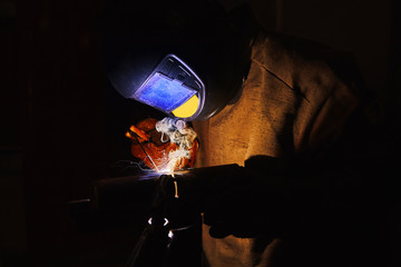 Close-up image of industrial worker at the factory welding steel structure on black background.