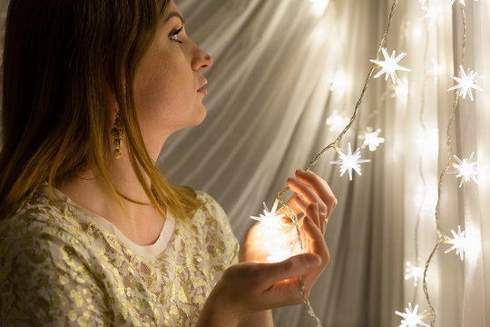 Portrait of a beautiful young white woman with brown hair holding an illuminated star shaped christmas chain of lights in her hands