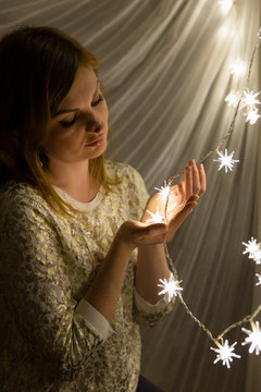 Portrait of a beautiful young white woman with brown hair holding an illuminated star shaped christmas chain of lights in her hands