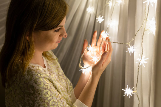 Portrait of a beautiful young white woman with brown hair holding an illuminated star shaped christmas chain of lights in her hands