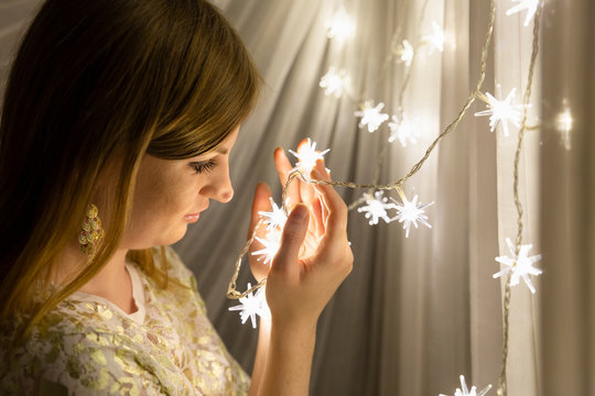 Portrait of a beautiful young white woman with brown hair holding an illuminated star shaped christmas chain of lights in her hands