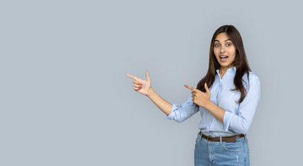 Excited overjoyed indian girl shopper looking pointing fingers aside isolated on grey studio background show copy space, amazed young woman customer happy by shopping sale offer, banner