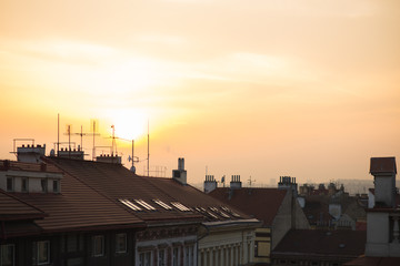 View of the roofs of historic buildings with red tiles during a bright sunset in Prague, Czech Republic.