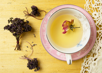 Cup of herbal tea in a porcelain cup with various herbs on yellow background. Tea with rose buds, tea with oregano.