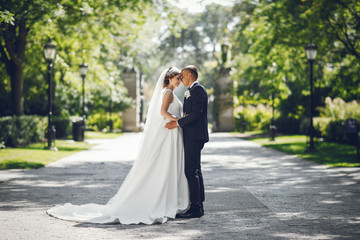 Elegant bride in a white dress and veil. Handsome groom in a blue suit. Couple in a summer park