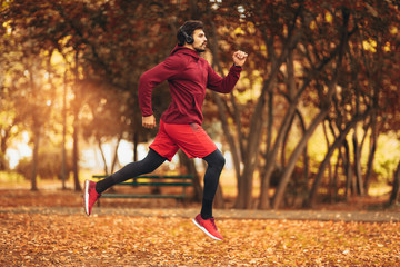 Young man running at park during autumn morning