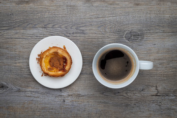 Traditional Portuguese Pastel de Nata tart with a cup of black coffee on a wooden table