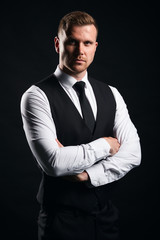 Confident young strong muscular bodyguard standing with crossed arms, isolated black background, studio shot.