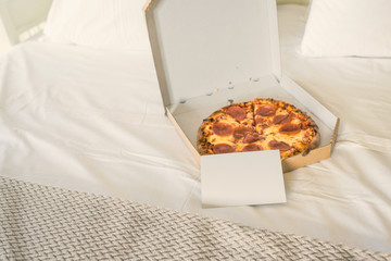 Open box of pizza on the big bed with empty card for text. Concept