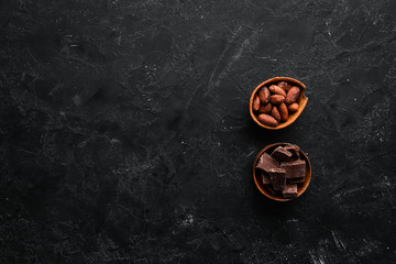 Chocolate and cocoa beans in a bowl. On a black stone background. Top view. Free copy space.